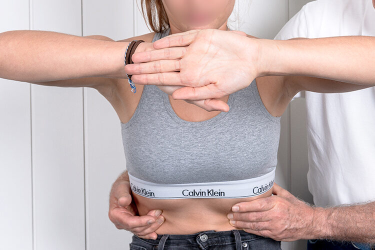 Top view of crop unrecognizable woman in casual wear showing chiropractor in eyeglasses and uniform pain spot on back while sitting on examination couch in hospital